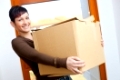 Woman lifting cardboard box while moving home, smiling.�