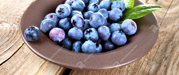 Fresh blueberries in bowl with leaves on wooden background