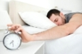 Sleeping handsome man being awakened by an alarm clock in his bedroom