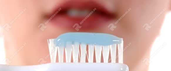 Zahnbürste vor dem verschwommen dargestellten Gesicht einer jungen Frau als Symbol für Zahnpflege