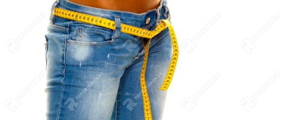 Eine junge, schlanke Frau in Jeans mit Massband nach erfolgreicher Diät