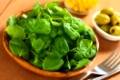 Fresh watercress on wooden plate with green olives and sweetcorn in the back and cutlery on the side (Selective Focus, Focus one third into the watercress)