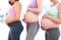 Pregnant women standing in a row looking at bumps in a fitness studio