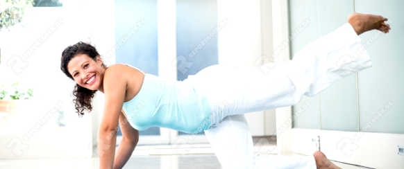 Full length portrait of smiling pregnant woman performing yoga on mat at fitness studio