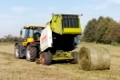 Ein Traktor vom Typ JCB Fastrac 3190 Plus mit einer Rundballenpresse vom Typ CLAAS Variant 280 bei der Heuernte auf einem Feld bei Dautschen in Sachsen. 