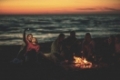 a group of friends using cell phones around the bonfire during autumn beach party drinking beer and having fun filter