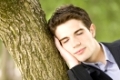 Junger Geschäftsmann schläft an einen Baumstamm gelehnt