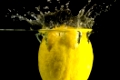 eine gelbe Zitrone fällt ins Wasser vor schwarzem Hintergrund