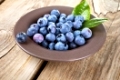 Fresh blueberries in bowl with leaves on wooden background