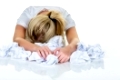 Eine junge Frau verzweifelt im Büro zwischen vielen Aktenordnern und zerknülltem Papier.Symbolfoto für Stress, Burnout und Überarbeitung.