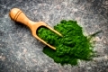 Green chlorella powder in wooden scoop.