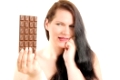 Erwachsene übergewichtige Frau mit schwarzen langen Haaren hält eine Tafel Schokolade in der Hand und überlegt sie zu essen, vor weißem Hintergrund.