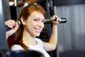 Attraktive junge Frau trainiert im Fitnesscenter an einer Schulterpresse