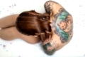 Redhead girl with wet hair sits in the bath full of water with milk and flower petals. She has a colorful fox tattoo on the back and another tattoos on her shoulders. Top view photo. Indoors.