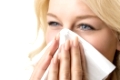 Portrait of a ill blond woman who is sneezing in a tissue