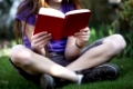 Ein Kind sitzt im Garten auf einer Wiese und  liest ein Buch
