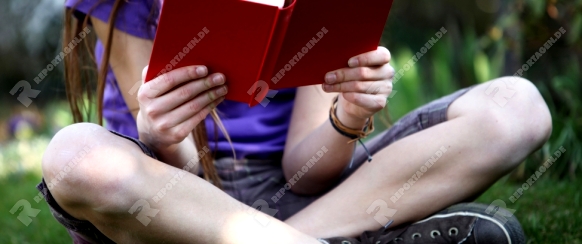 Ein Kind sitzt im Garten auf einer Wiese und  liest ein Buch