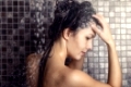 Woman shampooing her long brown hair under a shower working up a lather under the spray of water, view in profile