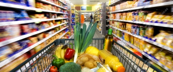 Shopping cart with foods between store shelves in a supermarket.
