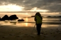 eine Frau mit Stativ am Strand fotografiert die Mitternachtssonne (Ramberg-Strand,Lofoten,Nordland,Norwegen)