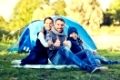 camping, tourism, hike and people concept - happy family over tent at camp site showing thumbs up gesture