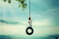 Young boy swinging on a tire over the foggy city with lake and forest background. Having fun and freedom concept