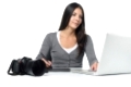 Female photographer smiling as she does her edits of her recently downloaded files on a laptop using a tablet and stylus with her camera alongside on the desk, over white