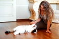 Beautiful woman playing with a cat on the parquet floor.