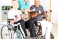 Physiotherapeutin mit zwei Senioren im Rollstuhl beim Training mit Hanteln