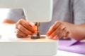 people, needlework and tailoring concept - tailor woman threading needle of sewing machine at studio